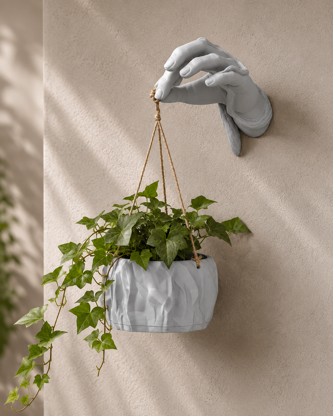 Sculptural hand wall mount holding a hanging marble-finish planter with fern